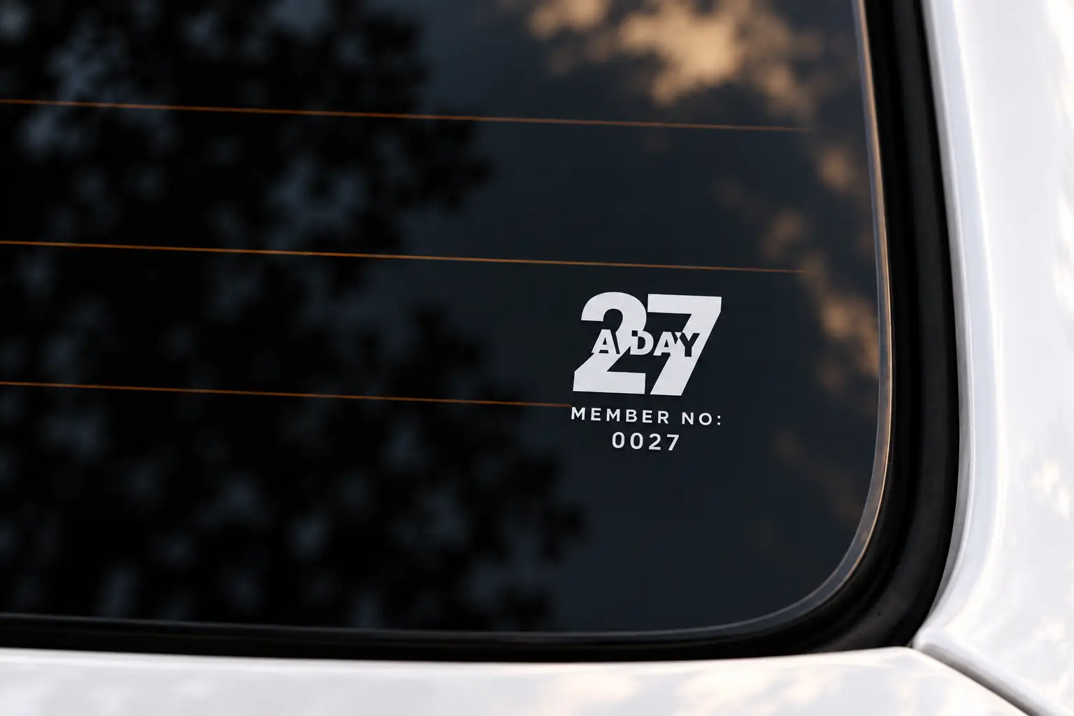 27aDay window sticker on the lower-right rear windshield of an unbranded white luxury sedan, with MEMBER NO: above 0027